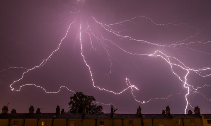 meerdere bliksemschichten boven een rijtje huizen tijdens ene onweersbui
